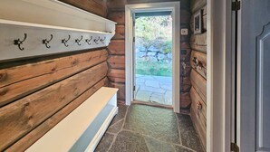 A wooden interior hallway with a bench, a door leading outside, and a stone-tiled floor.