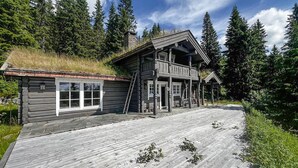 A rustic cabin with a wooden deck, a porch, and a stone foundation.