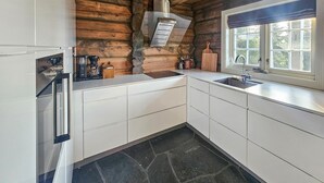 A kitchen with white cabinets, a stone backsplash, a built-in stove, and a window with a view of greenery.