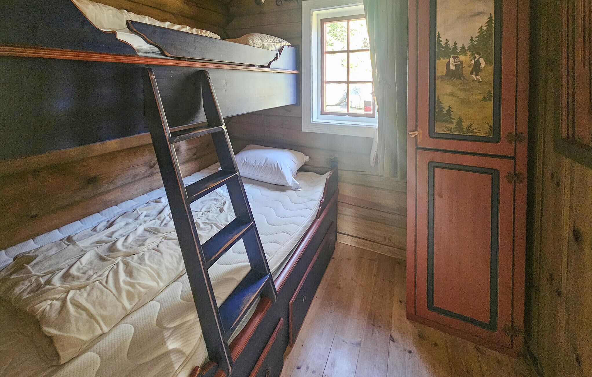 A bunk bed with a ladder, a window with a view of trees, and a door with a painting.