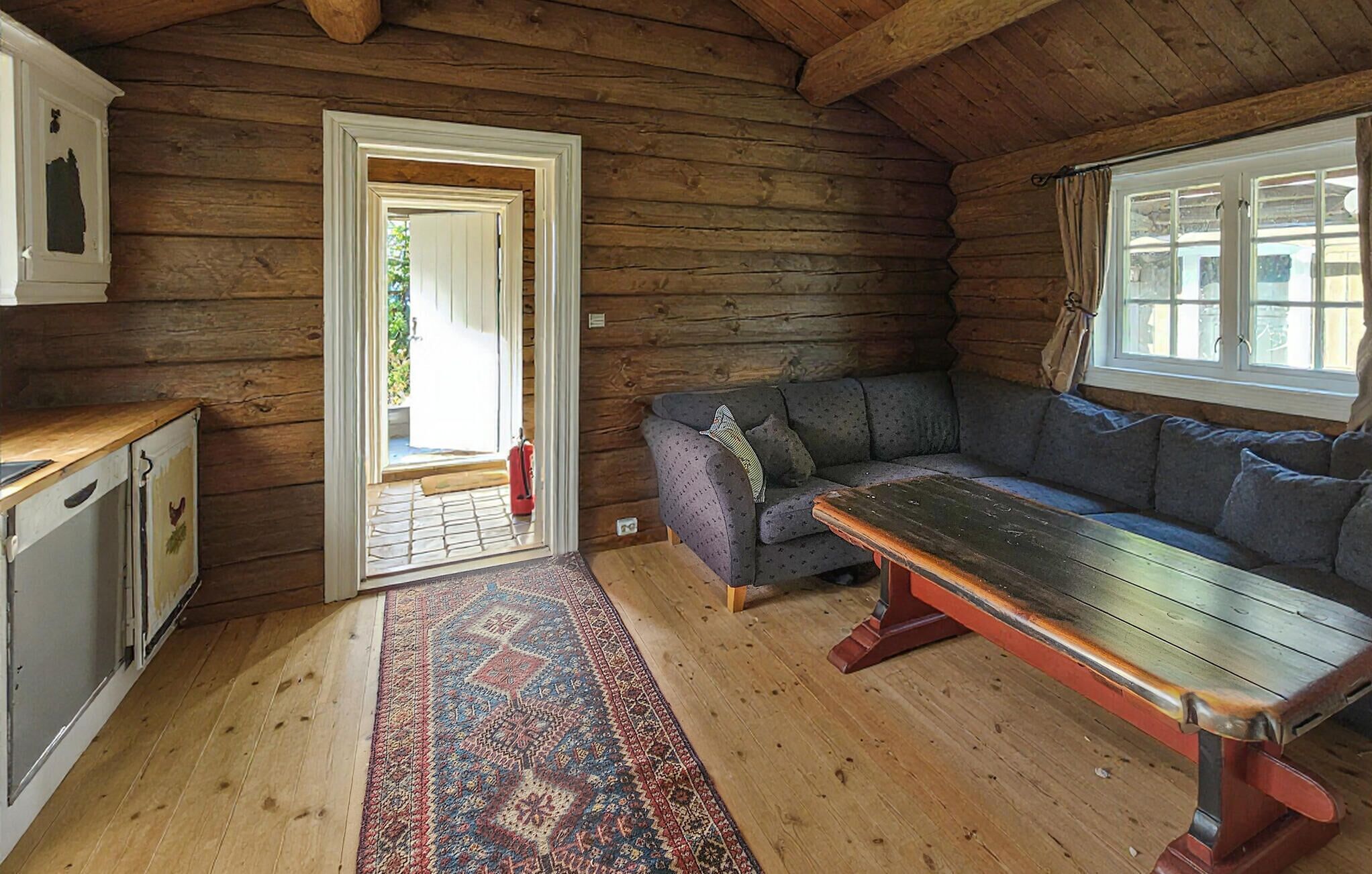 L’intérieur d’une cabane en rondins, avec un plancher en bois, un canapé, un banc et une porte donnant sur l’extérieur.