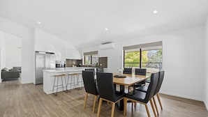 Une cuisine moderne avec des meubles blancs, un îlot central doté de tabourets et un coin repas avec une table en bois et des chaises noires.