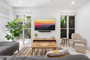 A modern living room with a large window, a flat-screen TV, a sofa, a coffee table, and a chair. - 44 Allura Circuit (Coolum Beach)