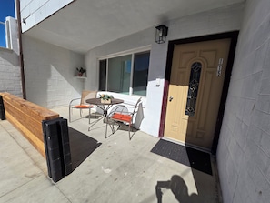 A patio with a wooden bench, two chairs, and a table.