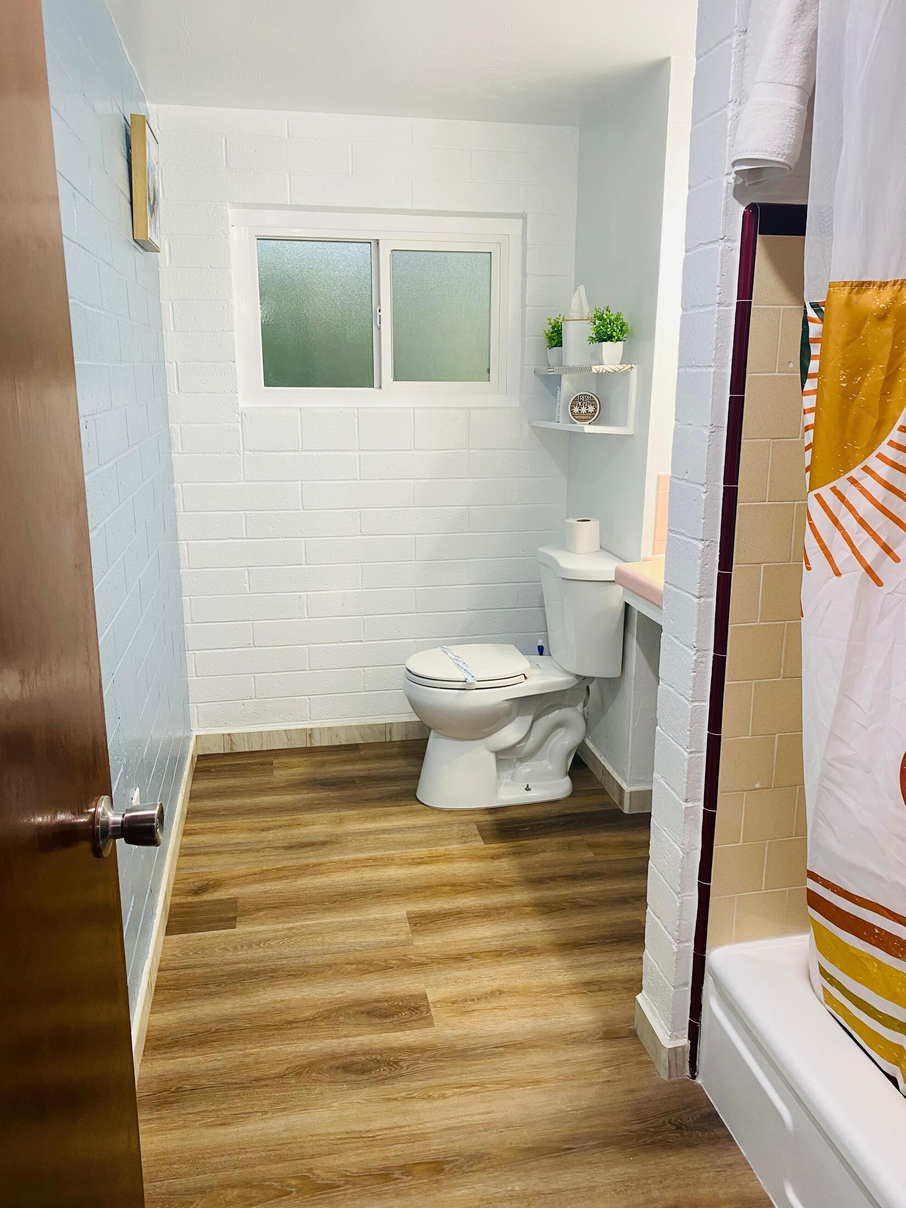 A bathroom with a white toilet, a window, and a shelf with toiletries.