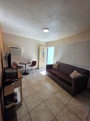 A living room with a sofa, a coffee table, and a TV stand with a poster.