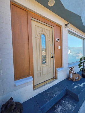 A beige door with a glass panel and a number plaque, a potted plant, and a deer statue on the steps.