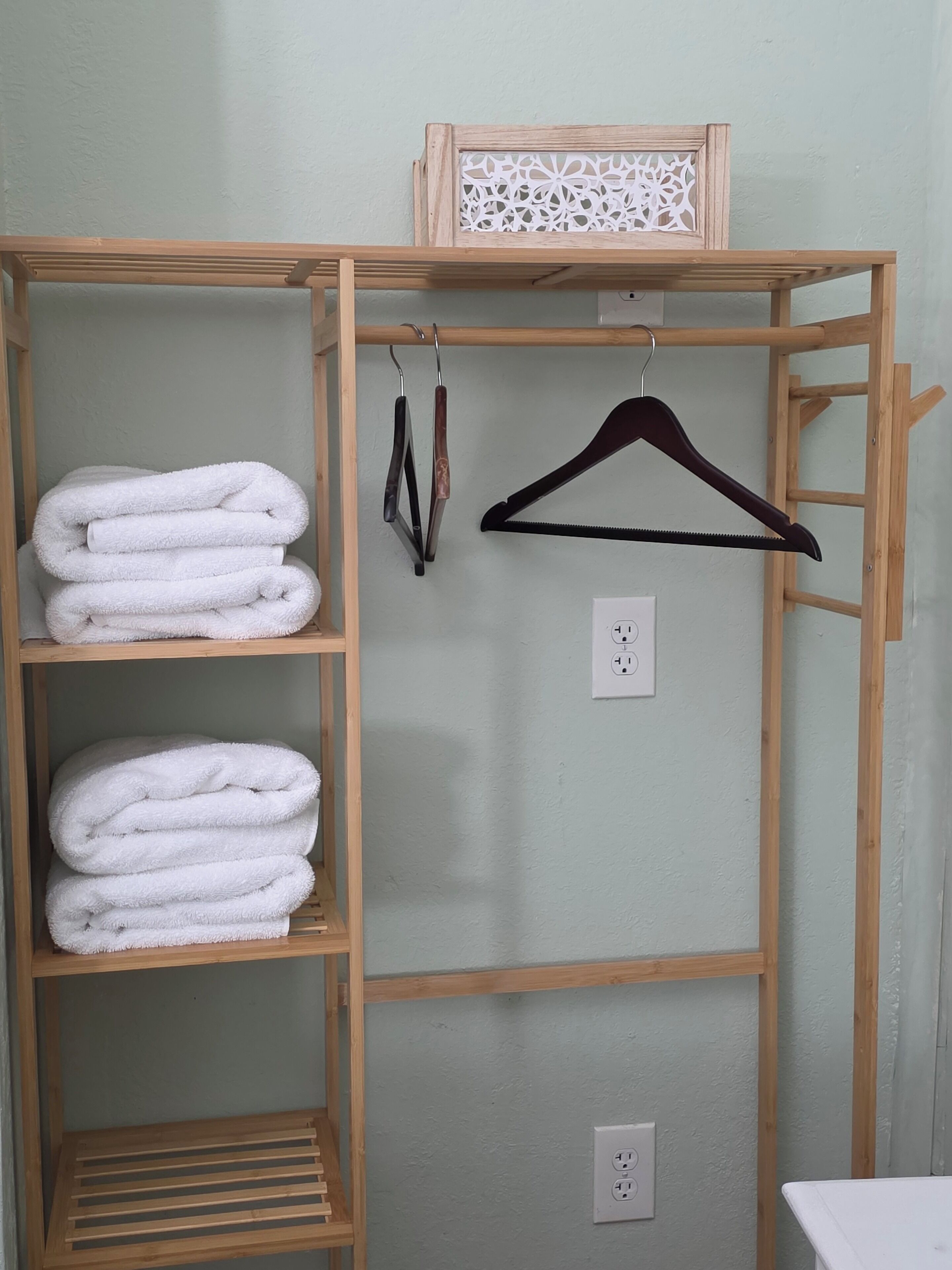 Un placard en bois avec des étagères où sont pliées des serviettes, un cintre en bois et une prise de courant.