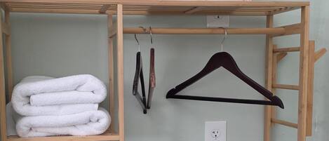 Un placard en bois avec des étagères où sont pliées des serviettes, un cintre en bois et une prise de courant.