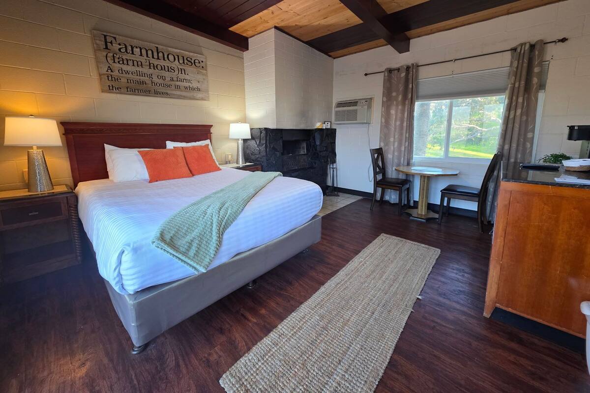 A bedroom with a large bed, a fireplace, a dining area, and a window with curtains.