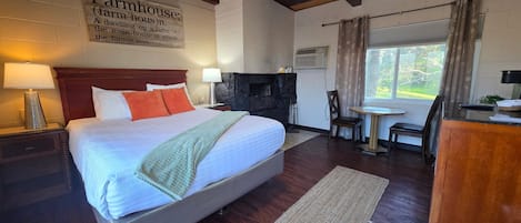 A bedroom with a large bed, a fireplace, a dining area, and a window with curtains.