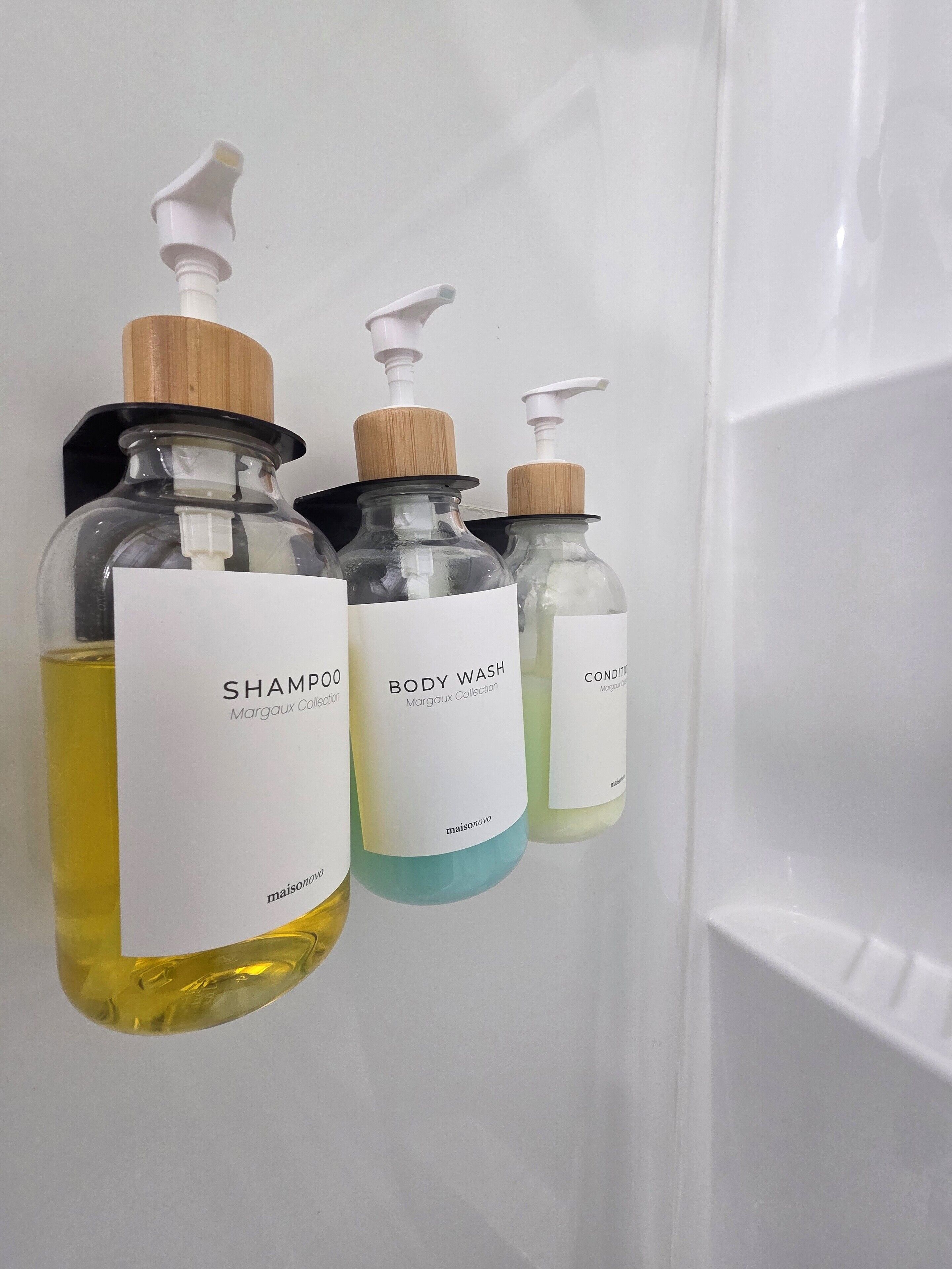 Three bottles of body wash hanging on a white wall.