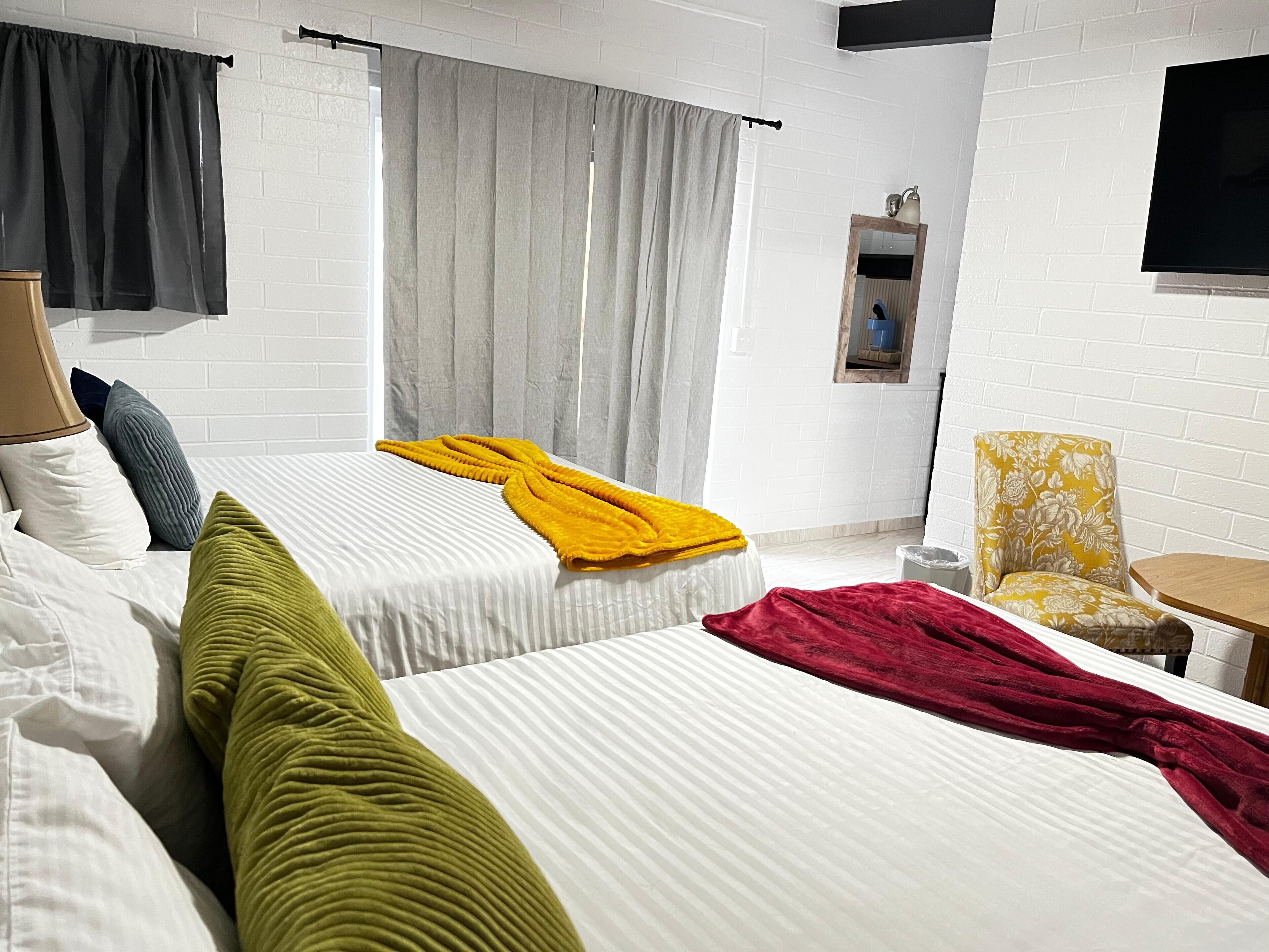 A hotel room with two beds, a small table, a chair, and a TV mounted on the wall.