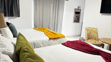 Habitación de hotel con dos camas, una mesita pequeña, una silla y un televisor montado en la pared.