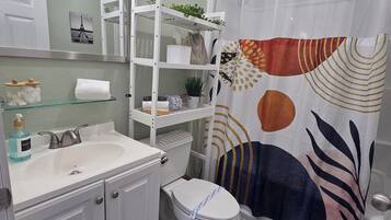 A bathroom with a white sink, mirror, and toilet. There is a shelf with toiletries and a shower curtain with a leaf pattern.