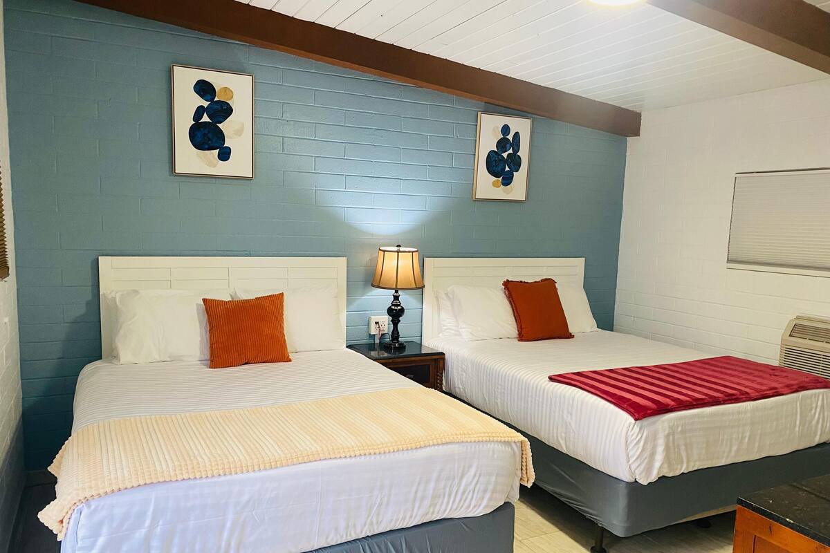 A room with two beds, a nightstand with a lamp, and artwork on the wall.