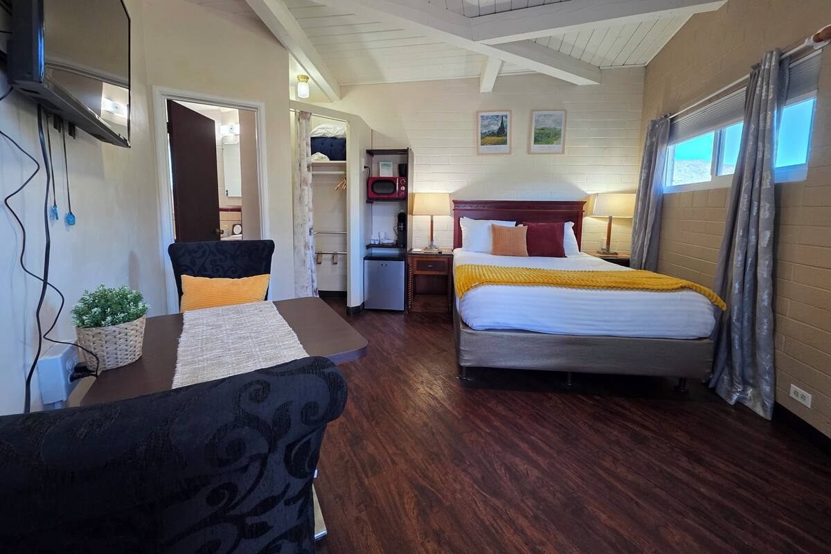 A hotel room with a bed, a desk, a chair, a wardrobe, a microwave, and a television.