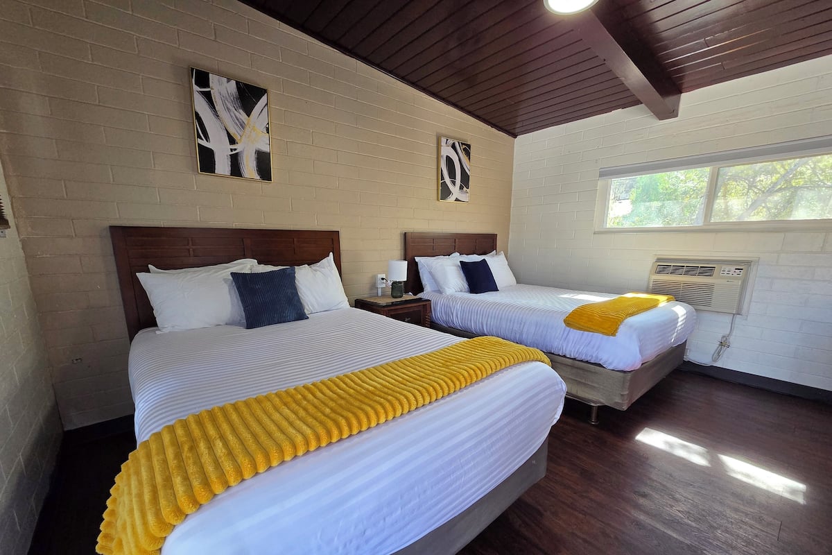 A hotel room with two beds, wooden headboards, white walls, and a window with a view.