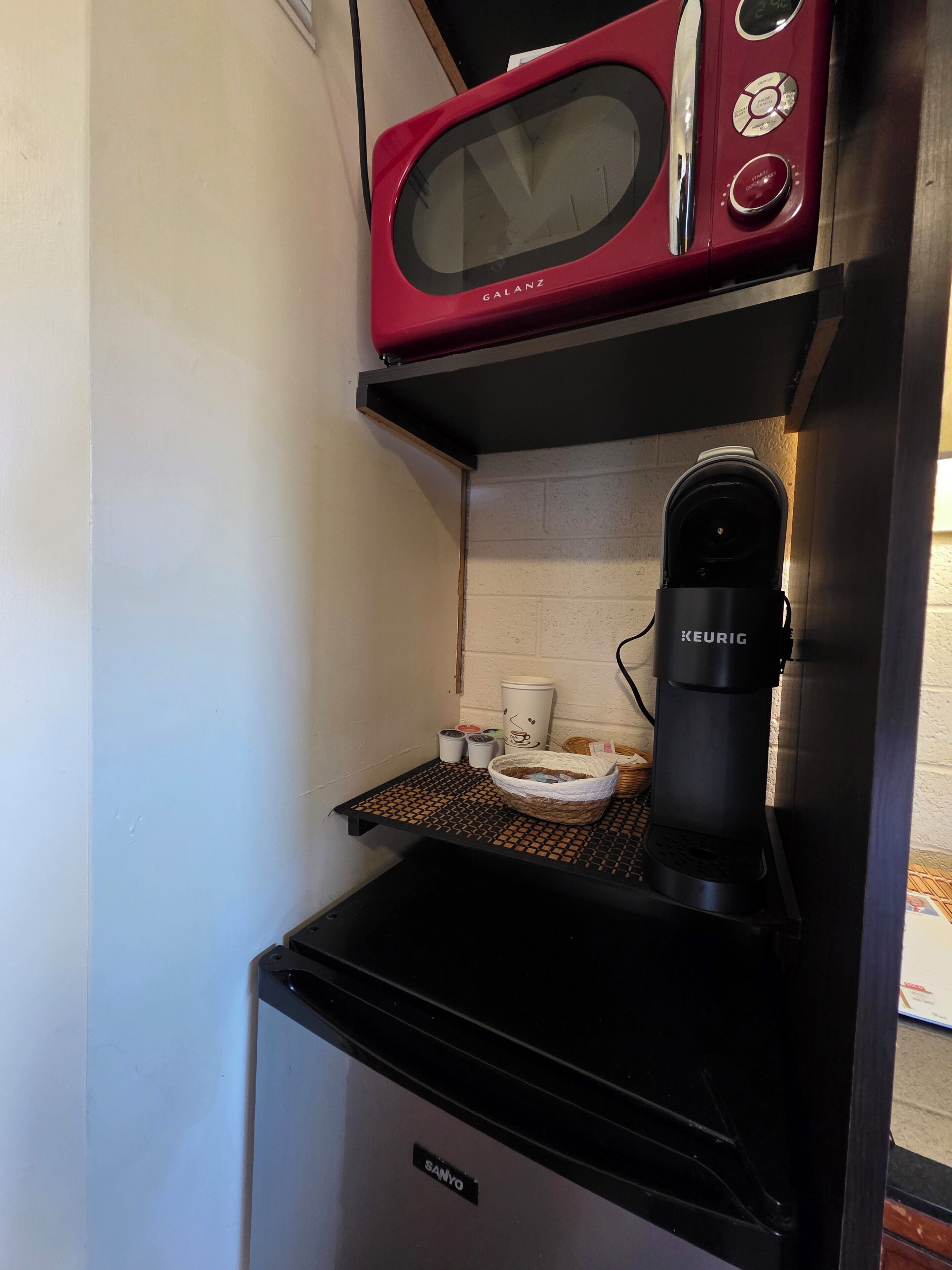 Pieni, käytännöllinen keittiö, jossa on punainen mikroaaltouuni, Keurig-kahvinkeitin ja Sanyo-jääkaappi.