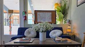 Ein Zimmer mit einem Holztisch, einem blauen Sofa mit weißen Kissen, einer weißen Vase mit Blumen und einer Karte an der Wand.