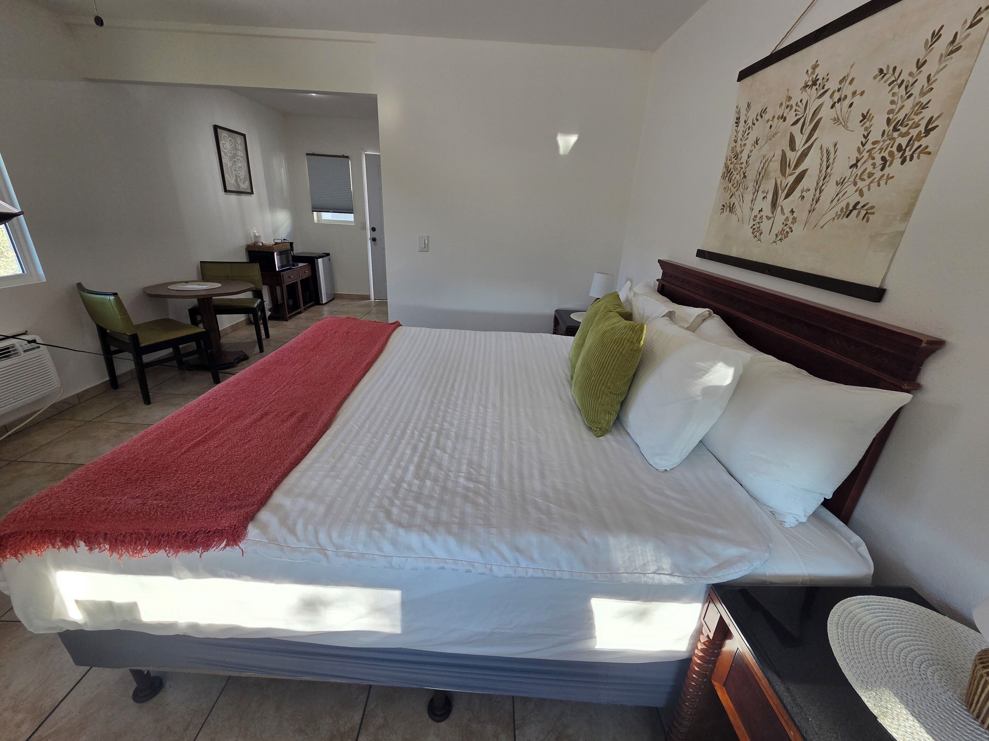 Habitación de hotel con cama, escritorio y silla. Se observa una ventana y una puerta en la habitación.