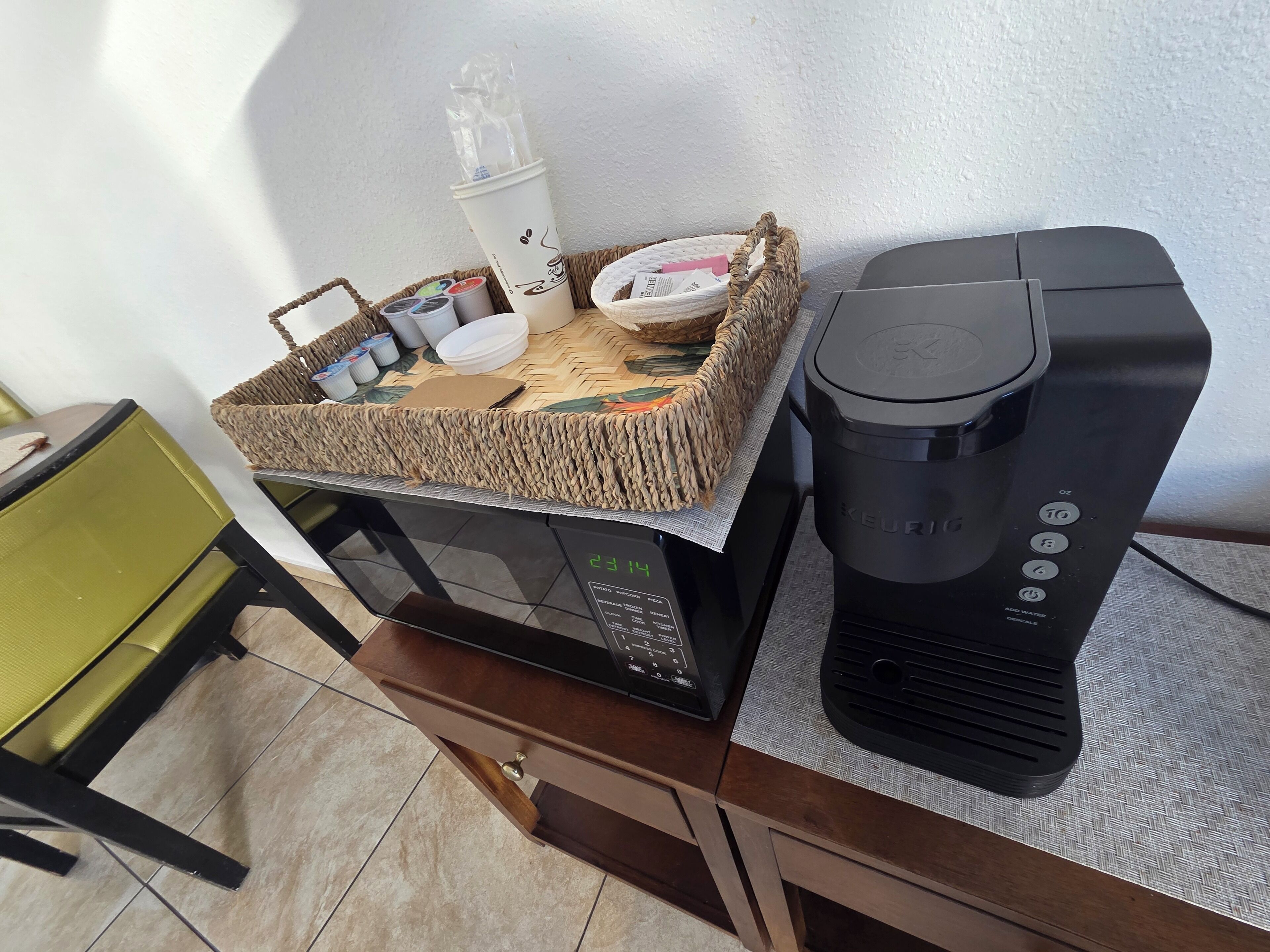 Una cocina equipada con microondas, cafetera y una cesta con tazas y licuadora.