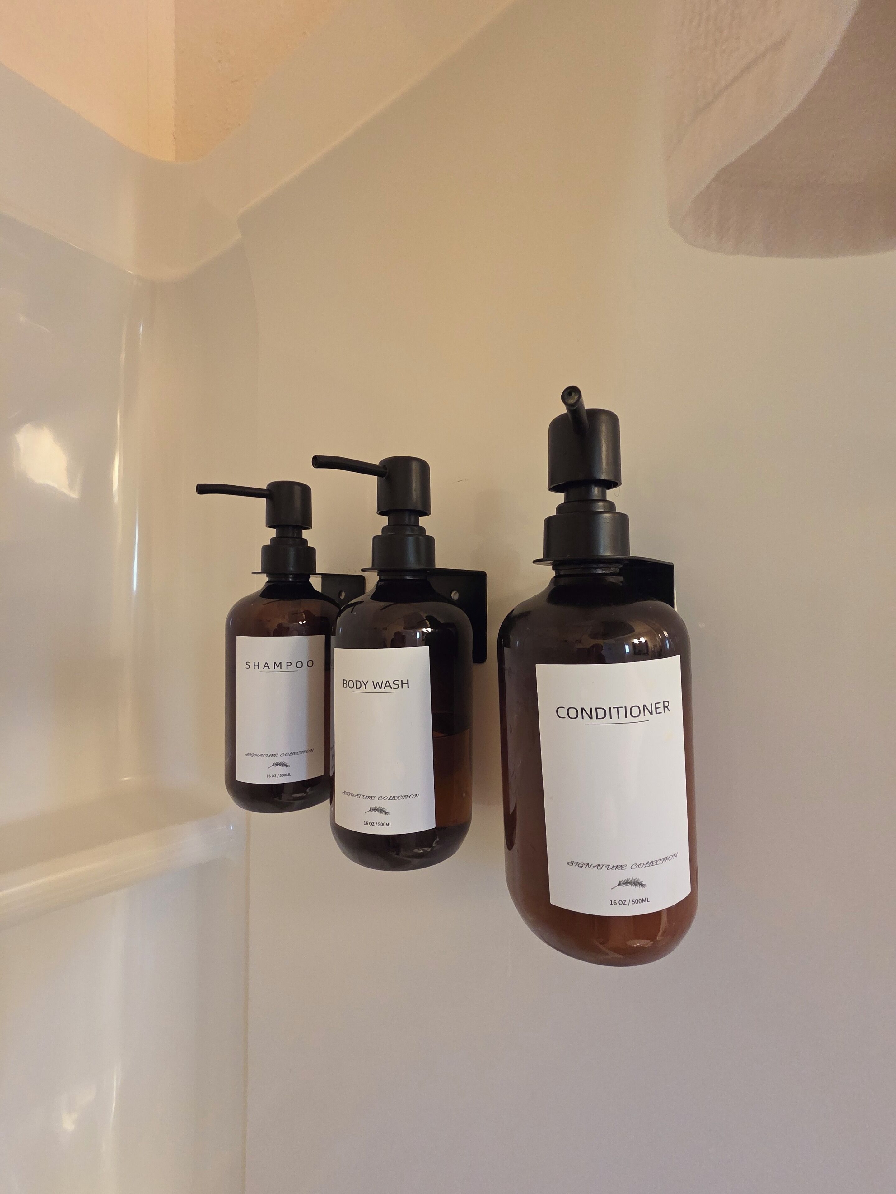 Three bottles of shampoo, body wash, and conditioner on a white wall.