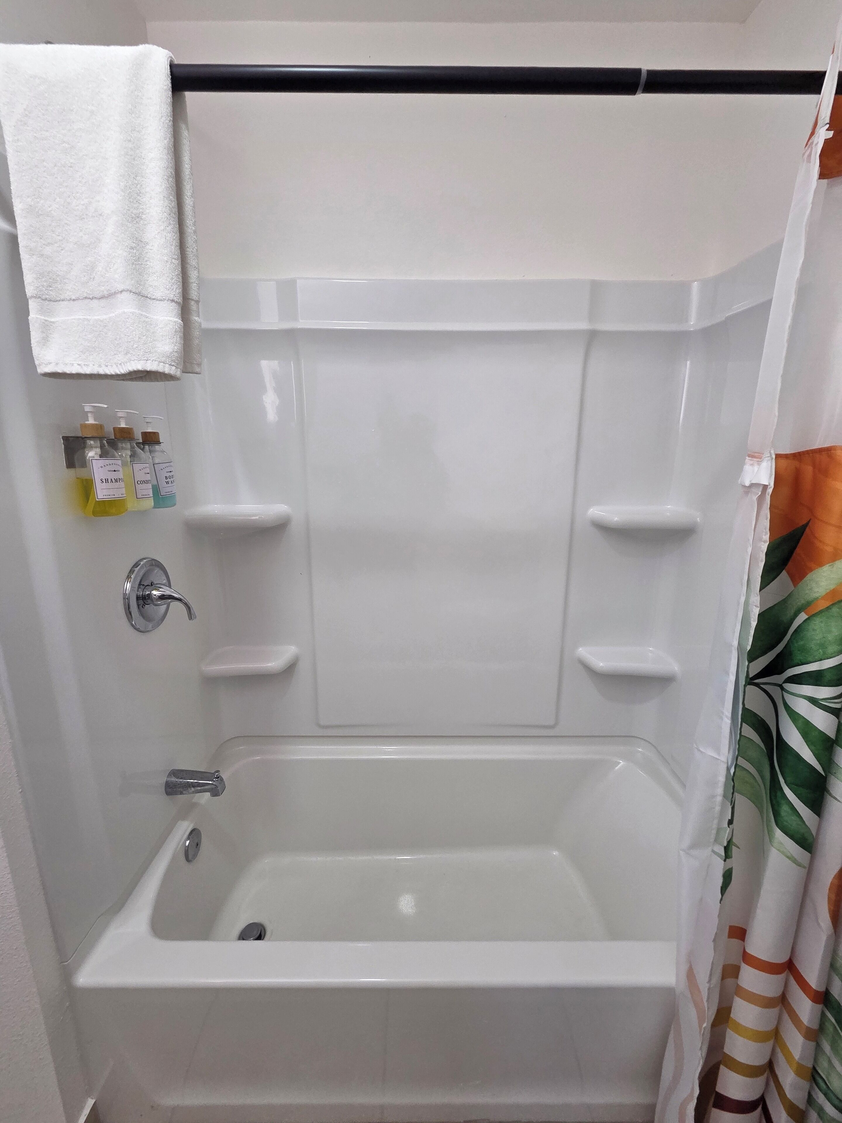 Um banheiro com banheira, uma toalha pendurada acima dela e três frascos de shampoo e condicionador.