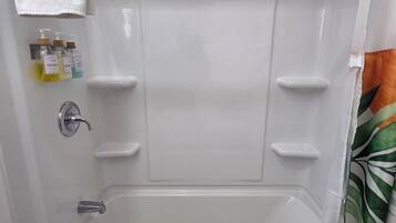 Um banheiro com banheira, uma toalha pendurada acima dela e três frascos de shampoo e condicionador.