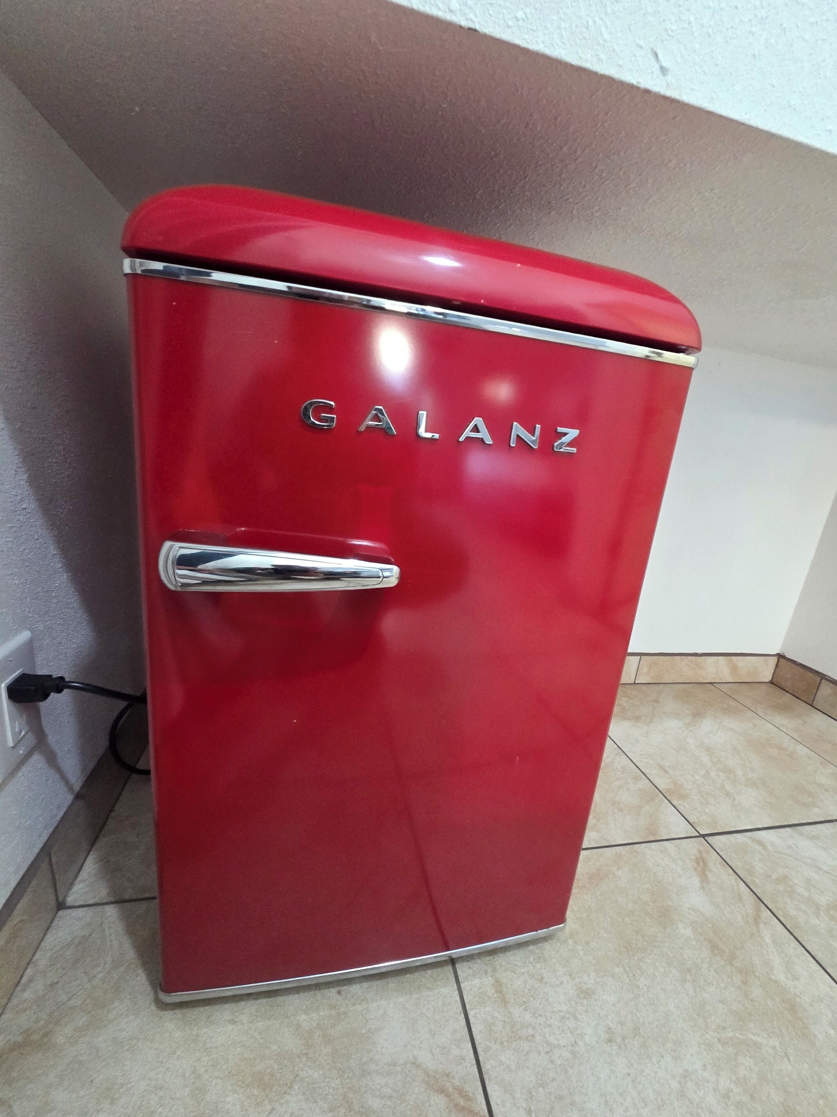 A red Galanz refrigerator with a chrome handle, located in a corner with tiled flooring.