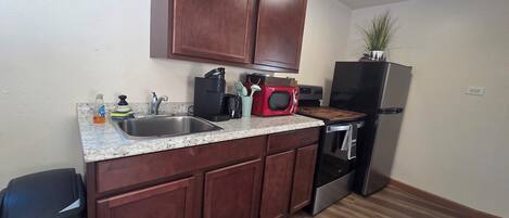 A compact kitchen with wooden cabinets, a stainless steel sink, a microwave, a toaster, and a refrigerator.