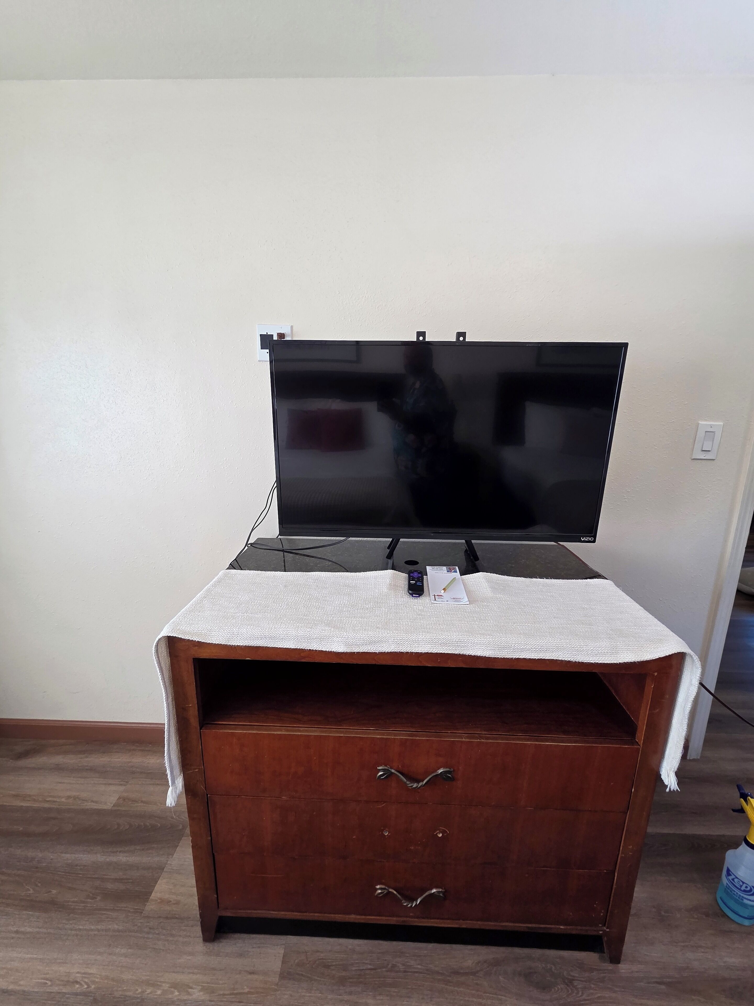 Un mueble de madera con un televisor de pantalla plana encima, un paño blanco en la parte frontal y un objeto pequeño en el estante.