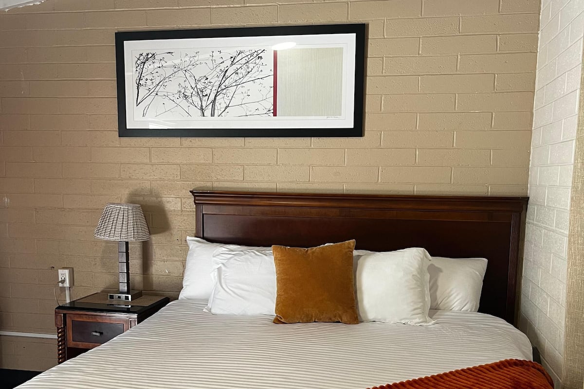 A neatly made bed with white and brown bedding, a red throw blanket, and a framed artwork above it.