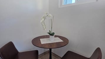 A small, round wooden table with two brown chairs, a potted orchid, and a window with a blind.