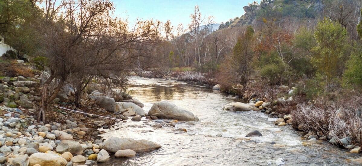 Un río serpentea a través de un paisaje rocoso con árboles y colinas al fondo.