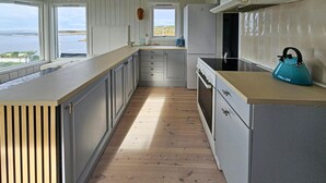 Une cuisine étroite avec un plancher en bois, des armoires grises et une vue sur l’eau par les fenêtres.