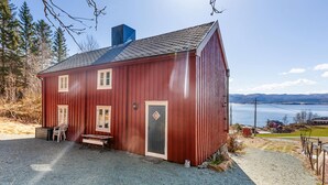 A red wooden house with a gravel driveway, a bench, and a door with a diamond-shaped window.