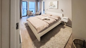 A modern bedroom with a large bed, a bedside table, a chair, and a view of the outdoors through large windows. - Stunning apartment in Tromsø with WiFi (Tromsø)