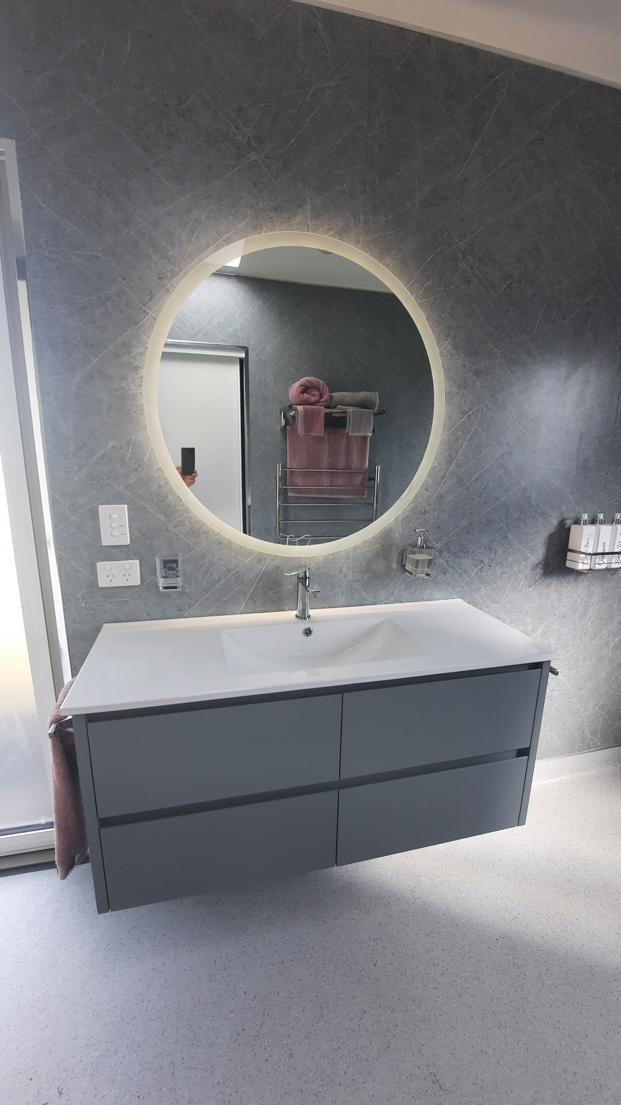 A bathroom with a large mirror, a white sink, and a towel rack with towels.