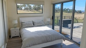 Une chambre à coucher avec un grand lit, deux tables de chevet, une fenêtre et une vue sur un champ verdoyant.