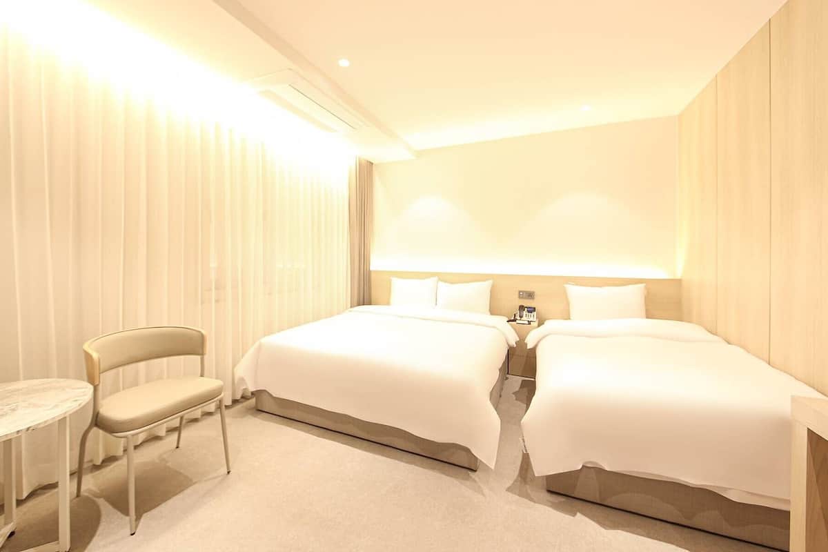 A hotel room with two beds, a desk, and a chair.