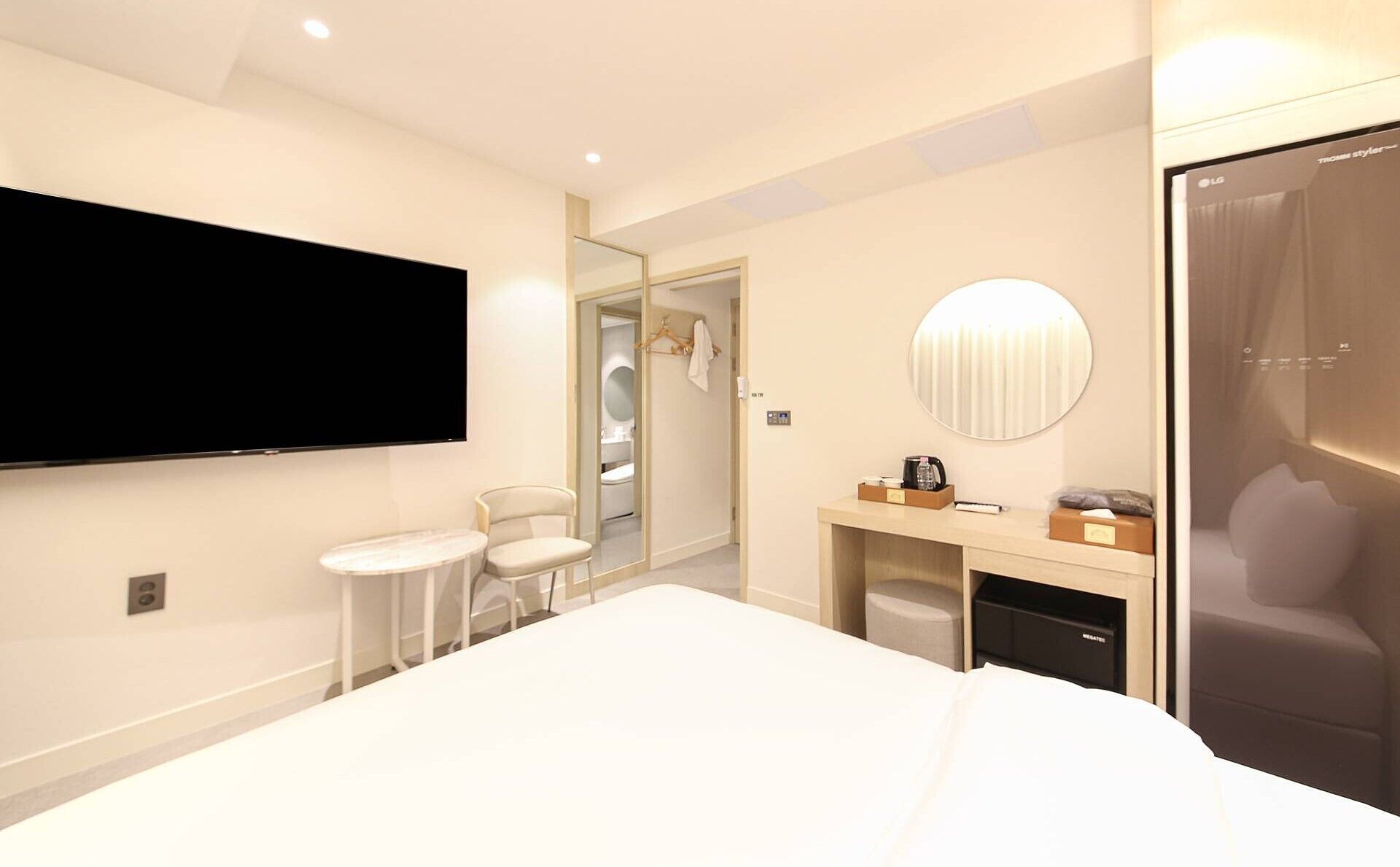 Un hotel moderno con una cama grande, un televisor montado en la pared, un espejo redondo pequeño, un escritorio con una silla y un vestidor.