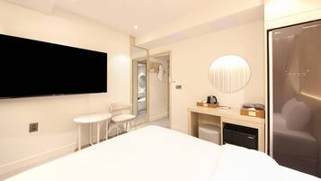 Un hotel moderno con una cama grande, un televisor montado en la pared, un espejo redondo pequeño, un escritorio con una silla y un vestidor.