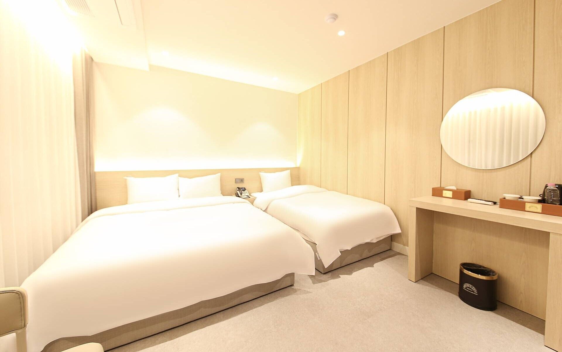 Une chambre d’hôtel avec un grand lit, des tables de chevet, un miroir rond et une poubelle.