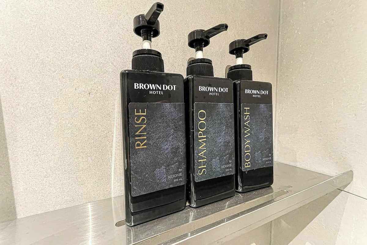 Three bottles of Brown Dot Hotel products: Rinse, Shampoo, and Body Wash, arranged on a shelf.
