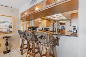 Una cocina moderna con armarios de madera, un refrigerador de acero inoxidable y una zona de bar con sillas de mimbre.