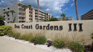 Skilt for Sea Coast Gardens III, der viser en bygning med flere etager, altaner og palmer.