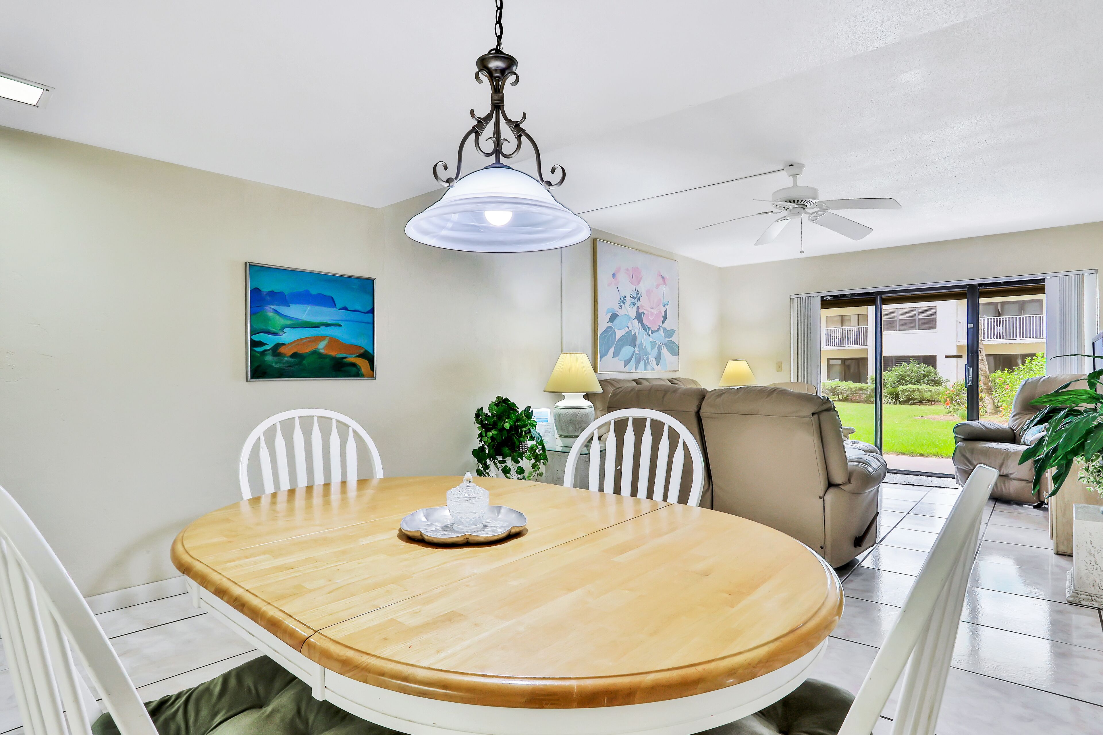 A dining area with a wooden table, white chairs, a chandelier, and a ceiling fan.
