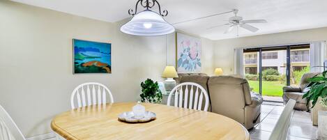 A dining area with a wooden table, white chairs, a chandelier, and a ceiling fan.