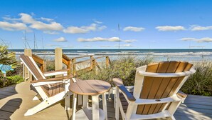 Un terrazzo in legno con poltrone Adirondack e un tavolino che si affaccia sull'oceano.